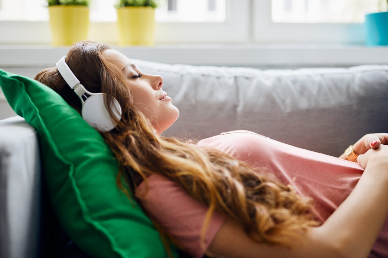 Why does listening to music make me tired? Woman listening to music asleep on sofa.