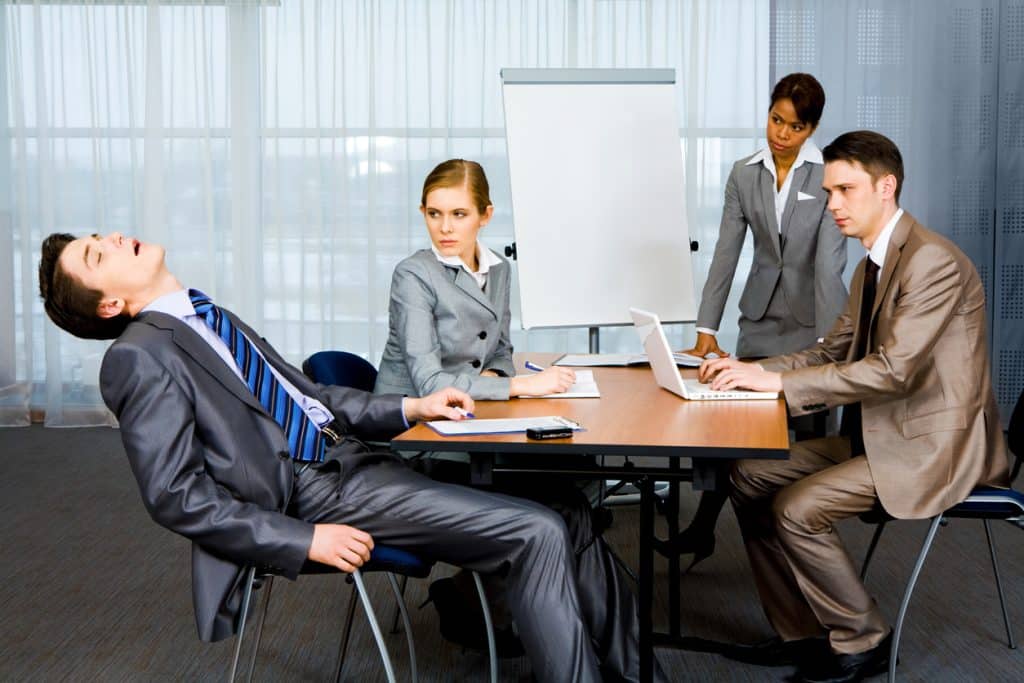 Why do I get sleepy in meetings? Man asleep in meeting room in front of colleagues.