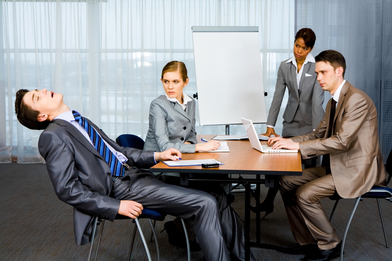 Why do I get sleepy in meetings? Man asleep in meeting room in front of colleagues.