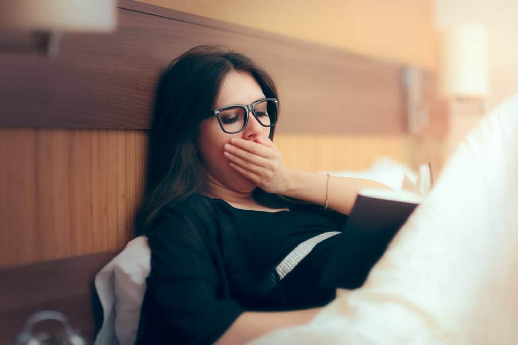 Why do I get sleepy reading books? Tired woman reading book in bed.